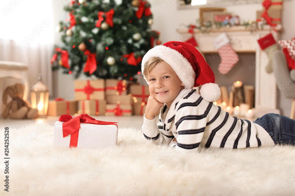 Cute little child in Santa hat with Christmas gift box at home