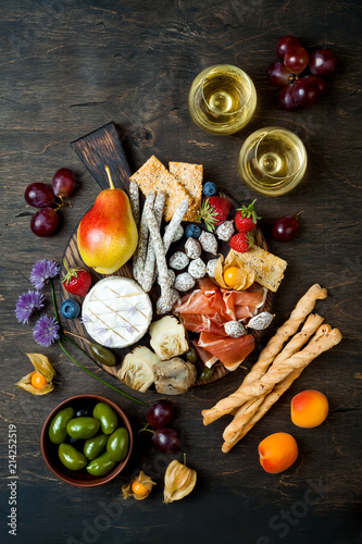 Appetizers table with italian antipasti snacks and wine in glasses. Cheese and charcuterie variety board over rustic wooden background