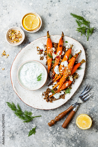 Roasted carrots lentil salad with feta, herb yogurt and dukkah on a light concrete background. Vegetarian food. Top view, flat lay photo