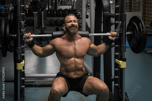 Hombre fuerte con grandes músculos haciendo sentadillas mientras entrena en el gimnasio. Ponerse en forma.