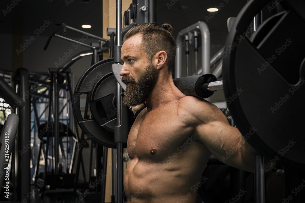 Hombre fuerte con grandes músculos haciendo sentadillas mientras entrena en el gimnasio. Ponerse en forma. Hombre fuerte con grandes músculos haciendo sentadillas mientras entrena en el gimnasio. Ponerse en forma.