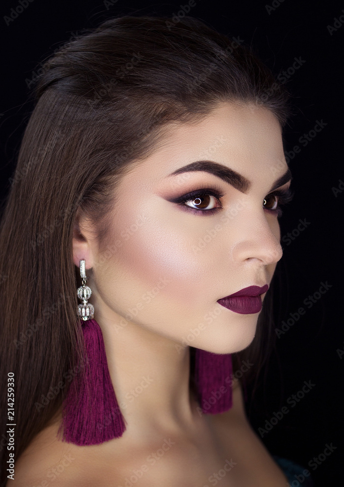Fototapeta premium Beautiful brunette with long earrings on a black background.