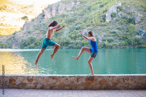 Side view of young people jumping and doing yoga on embankment at turquoise lake  