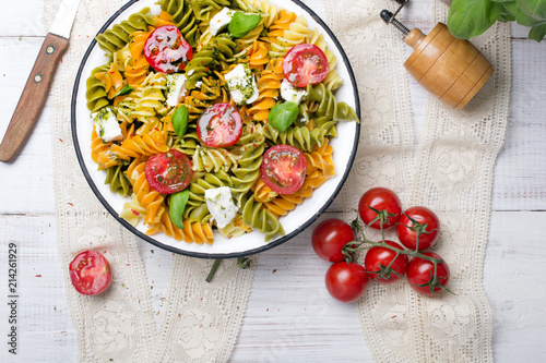 Włoskie jedzenie - Sałatka z kolorowym makaronem, pomidorami koktajlowymi, serem feta i świeża bazylią na białym drewnianym tle. 