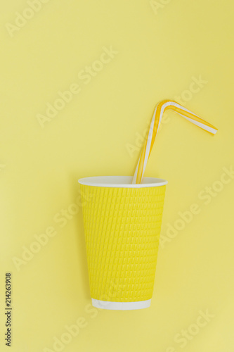 Abstract view of a paper cup for coffee with cocktail straw. Yellow background.