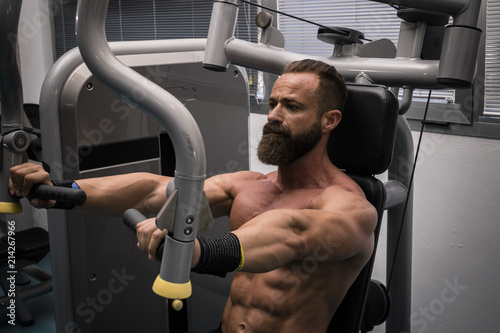 Hombre fuerte con grandes músculos entrenando pecho en el gimnasio. Ponerse en forma. © Trepalio