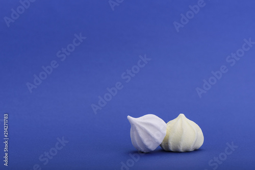 White and yellow meringues isolated on blue background with space for text