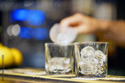 Barman pours ice into a glass. Ice cubes in an empty glass  dark background  front view with details.