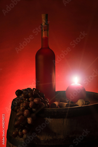 Butelka czerwonego wina w świetle świecy na beczce z winogronem.