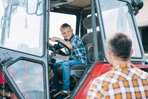 selective focus of father looking at happy son sitting in tractor