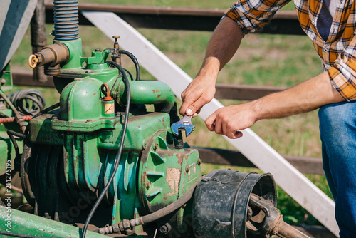 cropped shot of farmer holding wrench and fixing engine