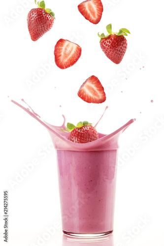Fotografia Delicious strawberries falling into a glass of strawberry milkshake / Fresh strawberries falling into a glass to make a delicious strawberry smoothie
