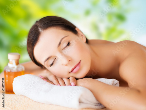 wellness, spa and beauty concept - close up of beautiful woman with bottle of massage or essential oil over green natural background