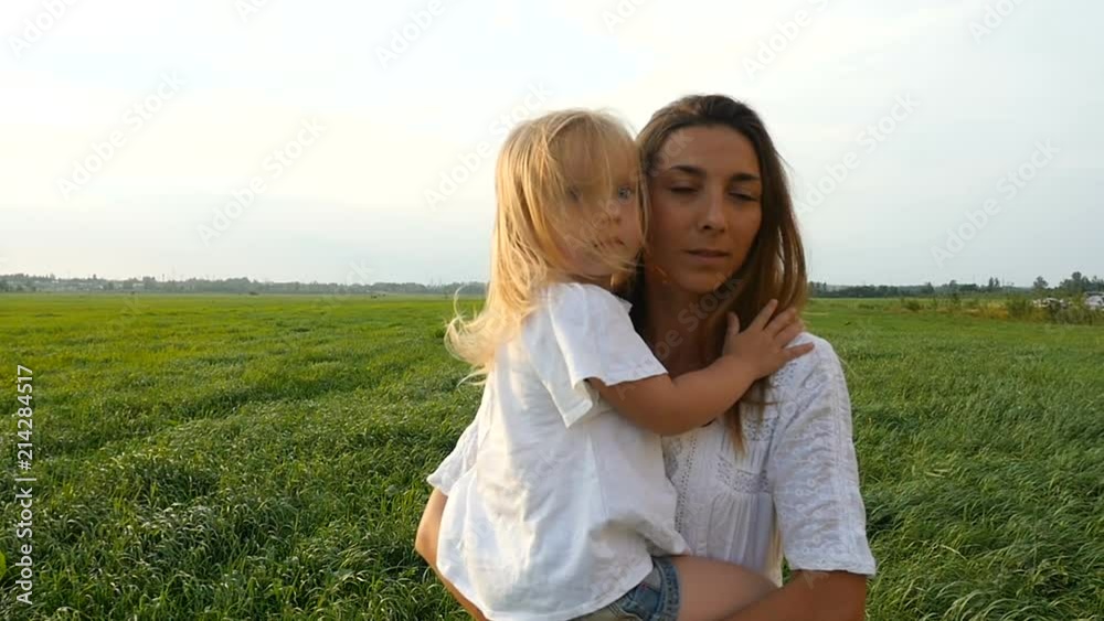 Happy family, mother and her little daughter walk on the green grass, summer evening. Mom with kid walking on green fields. Slow motion Happy family, mother and her little daughter walk on the green grass, summer evening. Mom with kid walking on green fields. Slow motion