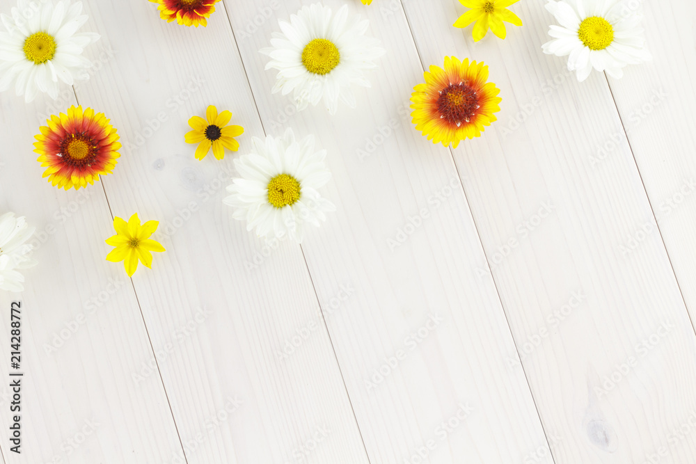 Obraz premium White daisies and garden flowers on a white wooden table. The flowers are arranged in the upper part, the empty space left below.