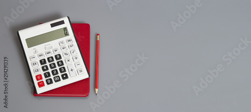 white calculator and red organizer on the grey table with red pencil