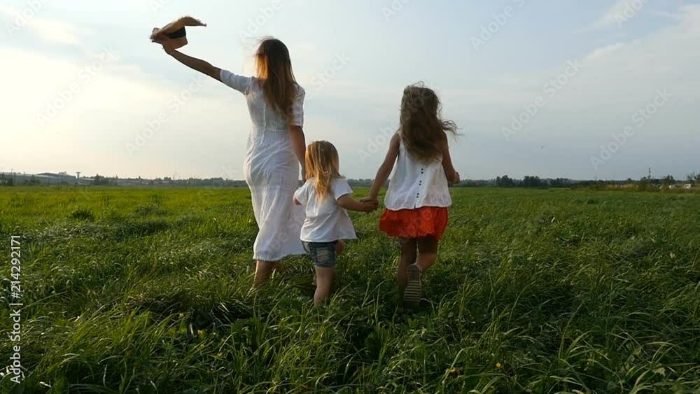 Cute family running on green grassy field. Young mother walks and runs with her little girls, children, on green grass. Slow motion Cute family running on green grassy field. Young mother walks and runs with her little girls, children, on green grass. Slow motion