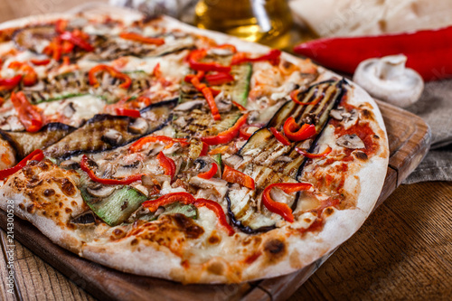 Delicious pizza with chicken, zucchini, eggplant, pepper, cheese and mushrooms on wooden rustic table. Top view. Toning.