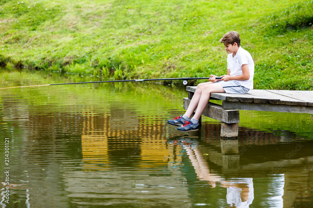 cute boy in white T shirt fishing in the lake and has fun, smiles. vacation with kids, holidays, active weekends concept cute boy in white T shirt fishing in the lake and has fun, smiles. vacation with kids, holidays, active weekends concept