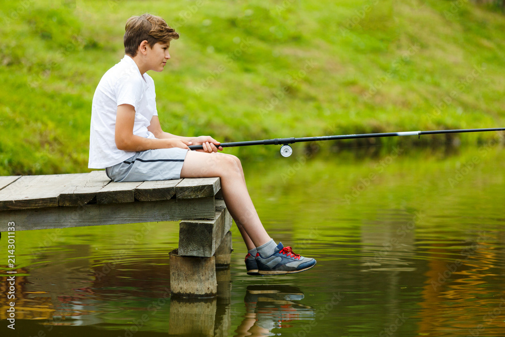 cute boy in white T shirt fishing in the lake and has fun, smiles. vacation with kids, holidays, active weekends concept