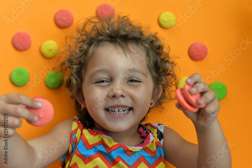 Little girl on an orange background with a colorful biscuit. Child with a cookie. Girl with a smile