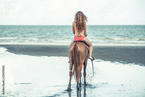 Woman fashion model riding a horse on the beach.