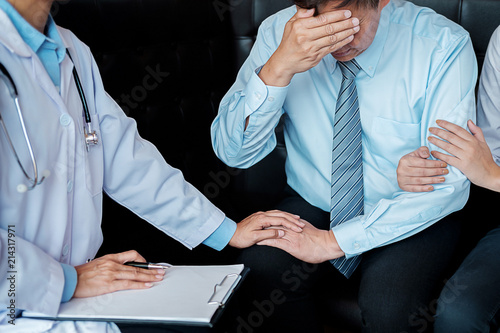 Patient listening intently to a male doctor explaining patient symptoms or asking a question as they discuss paperwork together in a consultation ..