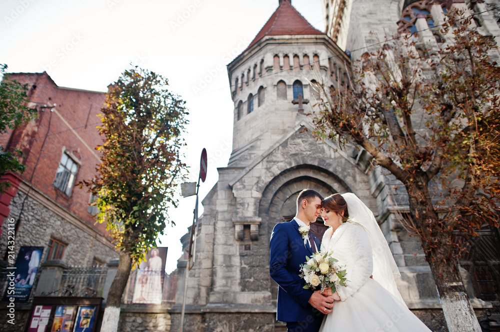 Newly married couple posing next to the old church in the town on a beautiful autumn wedding day. Newly married couple posing next to the old church in the town on a beautiful autumn wedding day.