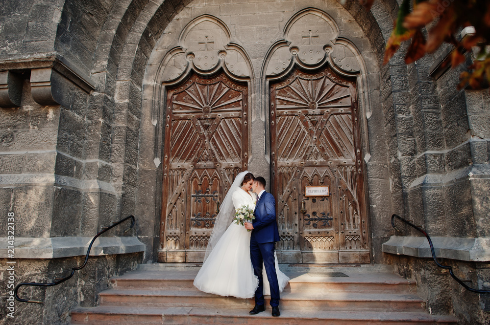 Romantic newly married couple kissing and posing by the ancient doors in an old town on their wedding day.