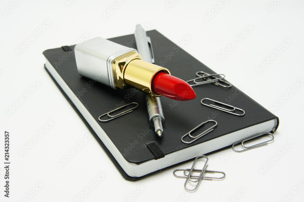 Lipstick, pen and paper clips on a black notebook. Lipstick, pen and paper clips on a black notebook.