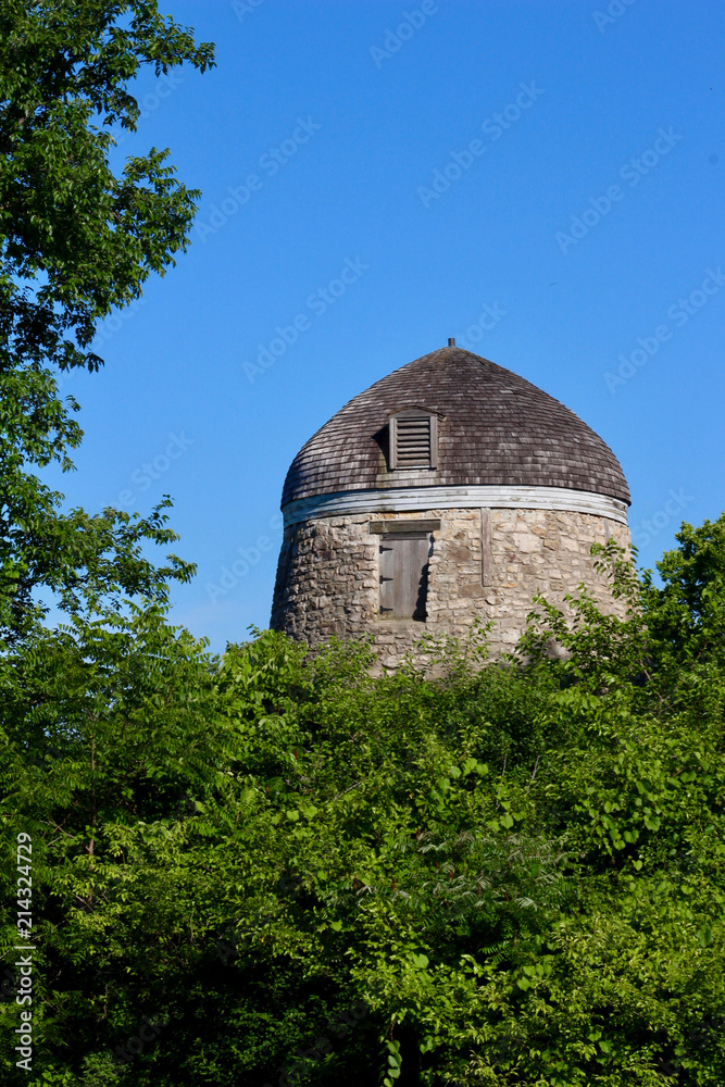 Fototapeta premium Old wind powered stone grist mill without it's original sails (windmill) with blue sky background
