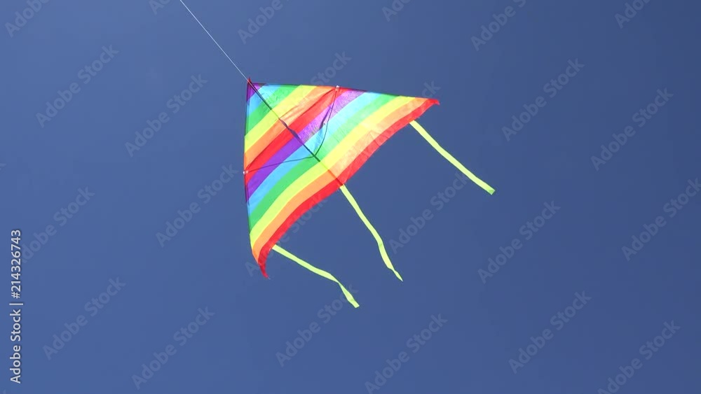 Colored kite flying free on blue sky, waving in the summer wind