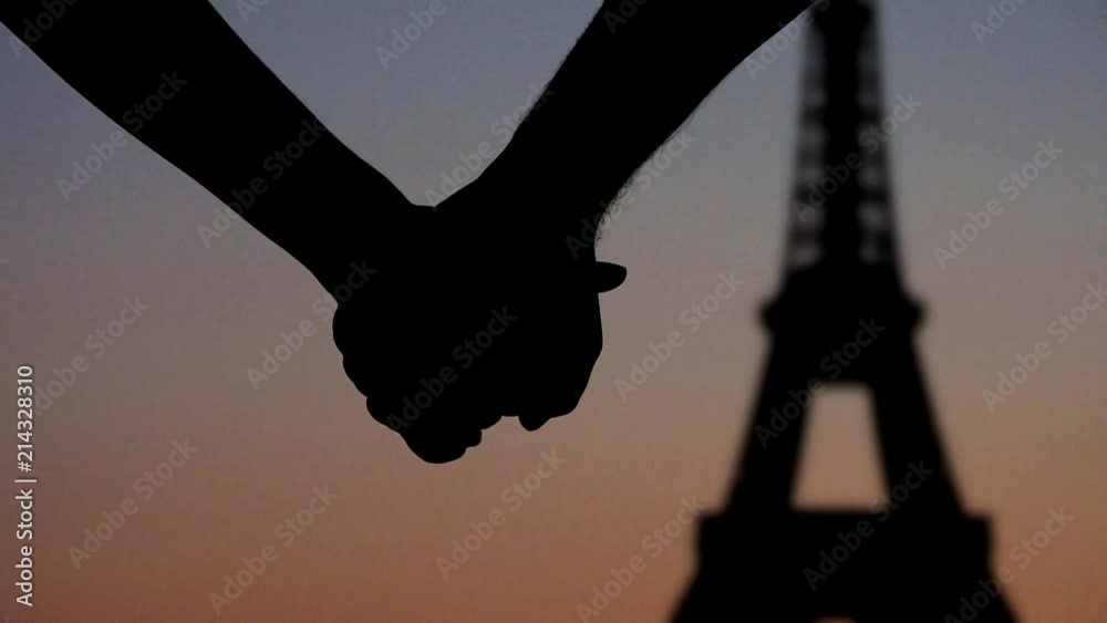 Young couple lovers joining hands in front of Eiffel tower Paris, silhouettes at sunset