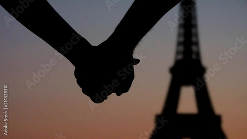 Young couple lovers joining hands in front of Eiffel tower Paris, silhouettes at sunset