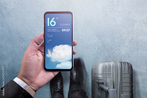 Mobile Technology for Traveling Concept. Top View of Businessman Walking with Suitcase, Holding Smartphone to Checking Weather Information in the Airport photo