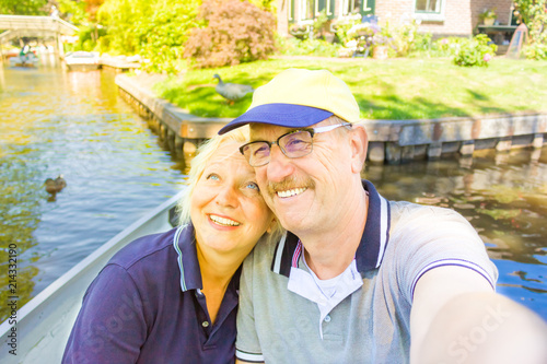 A retired couple is making selfie on the boat in Giethoorn canal (Netherlands) / old couple having fun in the Venice of North (Holland)