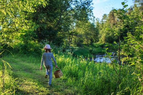 Young girl walking on a path through green woods carrying a birchbark basket