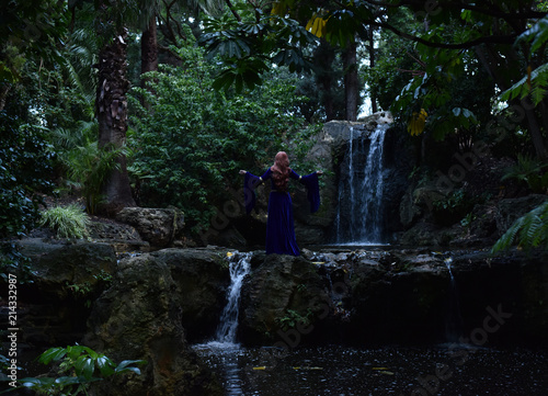 full length portrait of girl wearing long blue medieval gown. wandering through a forest landscape.