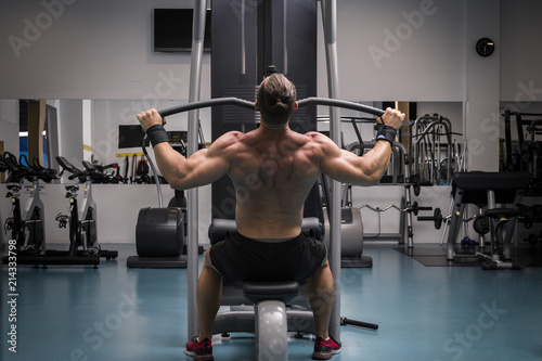 Hombre fuerte con grandes músculos entrenando jalón al pecho en el gimnasio. Ponerse en forma.