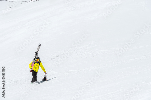 A skier in a helmet and mask with a backpack rises on a slope against the background of snow and a glacier. Backcountry Freeride