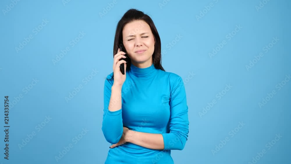 Unhappy and upset woman talking on the phone on blue background. Worried and stressed girl. Unhappy and upset woman talking on the phone on blue background. Worried and stressed girl.