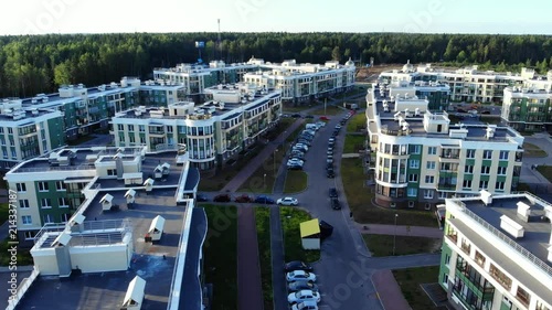 Flying over rooftops of modern apartment buildings, small town near forest