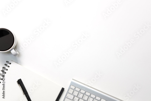Modern white office desk table with keyboard computer, coffee, pen and notebook paper with workspace top view workspace.