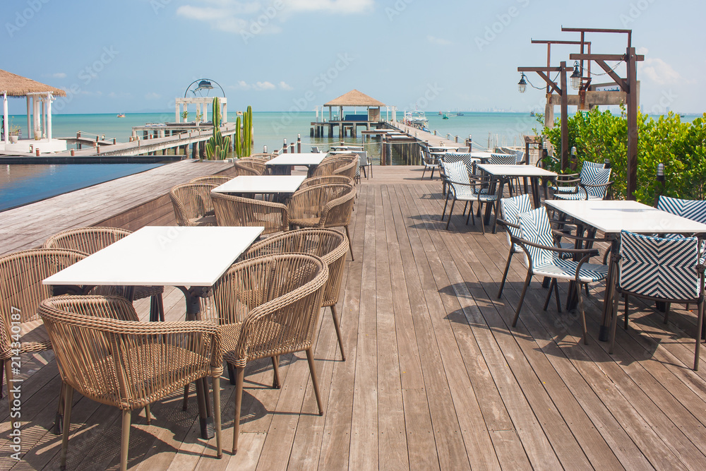 Rows of wooden chair and table locate on terrace of restaurant with seascape in the background.