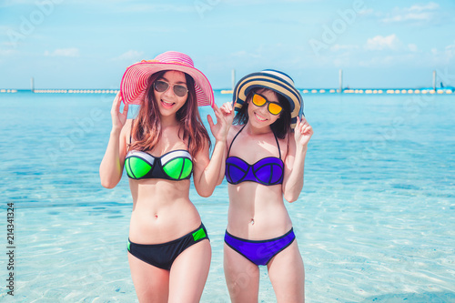Happy two asian woman on beach enjoying sun smiling under blue sky. Cheerful beautiful bikini girl sun tanning having fun on tropical beach.