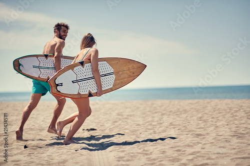 Happy man and woman surfers running together to surf at the beach .