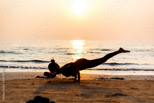 Young healthy woman practicing yoga on the beach at sunset