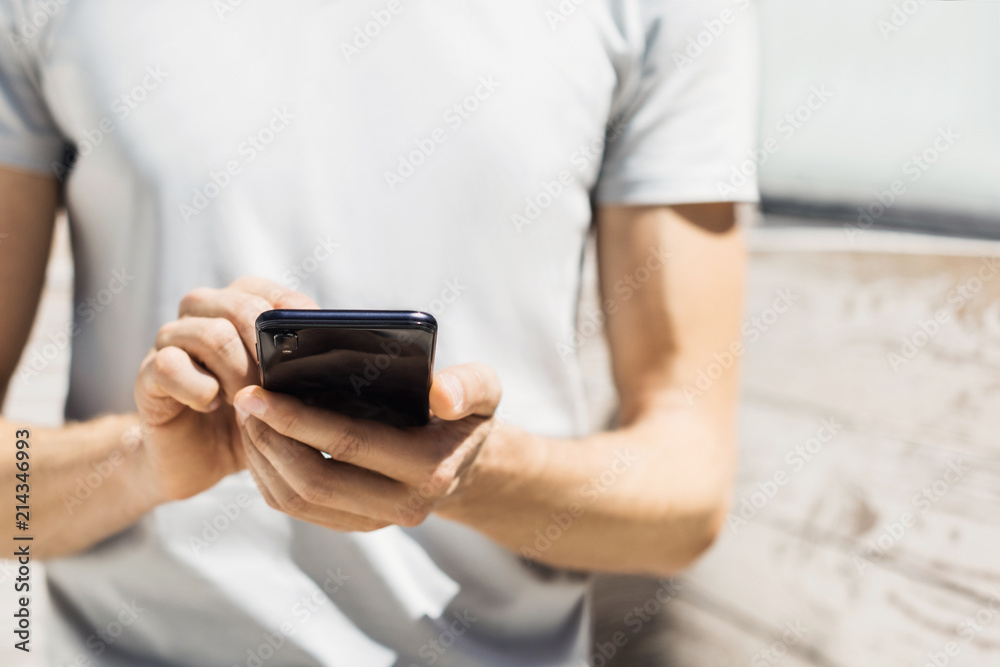 Young man texting on his smartphone in the city. Close up of hand using mobile phone outdoor Young man texting on his smartphone in the city. Close up of hand using mobile phone outdoor
