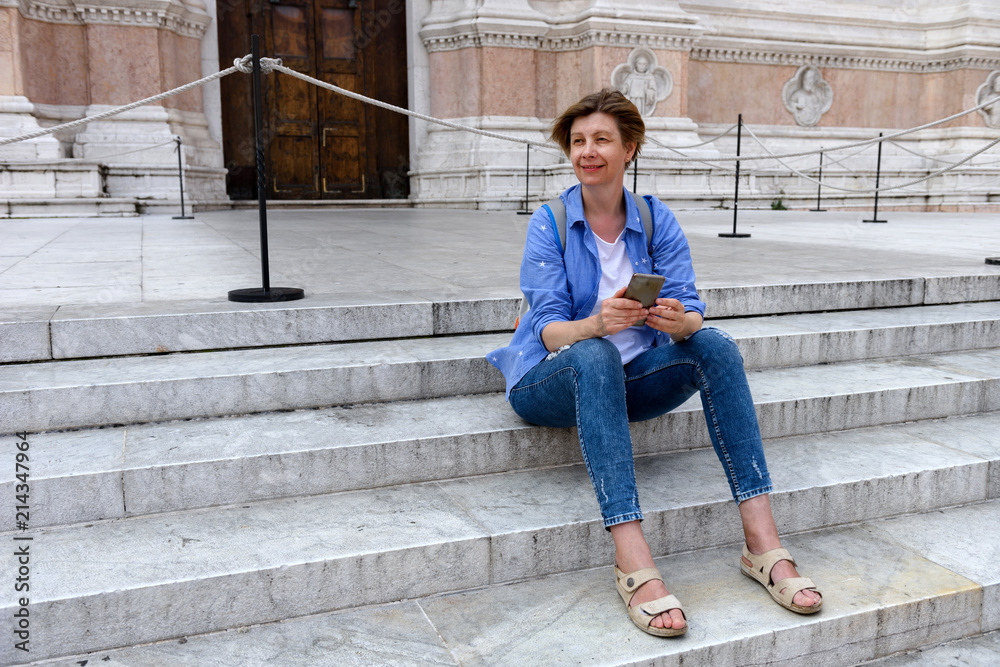 Slim, slender middle-aged woman, a tourist in Bologna, Italy. Sits on the steps of the Cathedral. Travel to Europe.