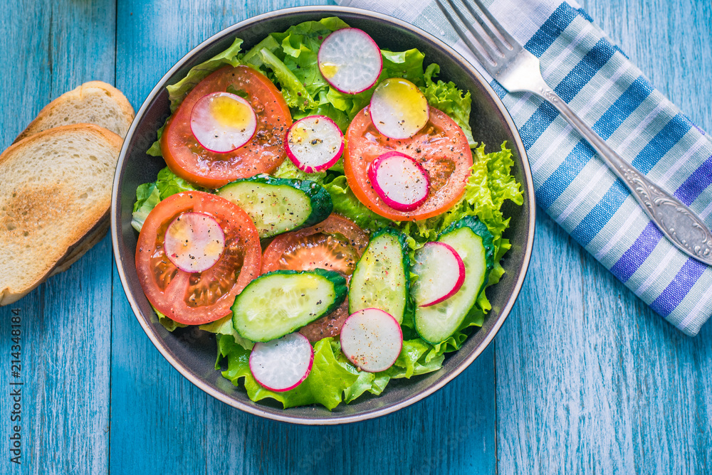 Healthy vegetarian salad with fresh tomatoes, cucumbers, onions, lettuce and radishes with olive oil on a rustic wooden background - top view